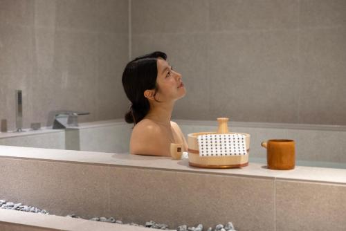 a woman is sitting in a bathtub with a container at Koum Ryokan Hotel Gijang by Aank in Busan