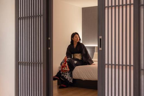 a woman sitting on a bed in a room at Koum Ryokan Hotel Gijang by Aank in Busan