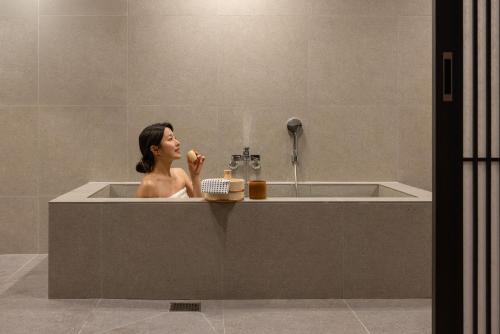 a woman is sitting in a bath tub at Koum Ryokan Hotel Gijang by Aank in Busan