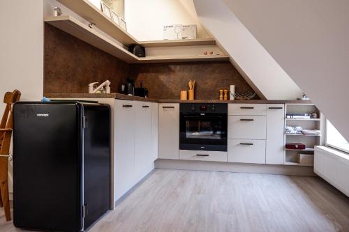 a kitchen with white cabinets and a black refrigerator at Malebný byt pod hradem Křivoklát in Křivoklát