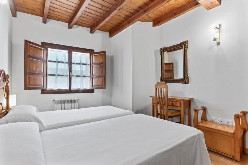 a white bedroom with two beds and a mirror at Apartamentos El Rincón de Bustio in Bustio