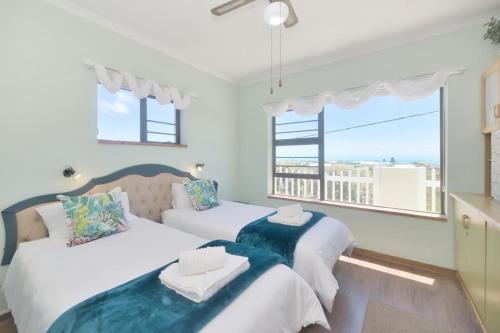 two beds in a room with two windows at Land's Edge Eco Friendly Cottages and Apartments in Struisbaai