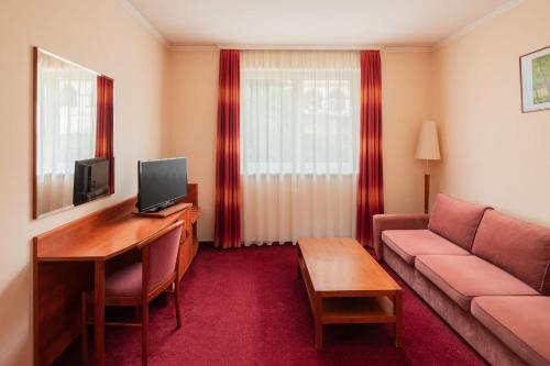 a living room with a couch and a desk with a television at Erzsébet Park Hotel in Parád