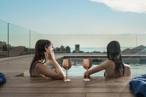 two women sitting next to a pool with wine glasses at WANDERLUST HOTEL - SUITE & SPA - APARTMENTS & VILLAS - Bardolino, Lago di Garda - Verona in Bardolino