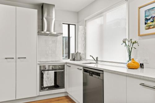 a kitchen with white cabinets and a stainless steel oven at Harakeke Whāre - Christchurch Holiday Homes in Christchurch