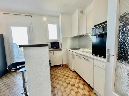 une cuisine avec des armoires blanches et des appareils noirs dans l'établissement Appart T3 - 200 m plage - Dernier étage vue mer et camargue, à La Grande Motte