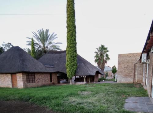 a building with a thatched roof and two palm trees at Vryburg Good Time Yafe Guest House in Vosburg