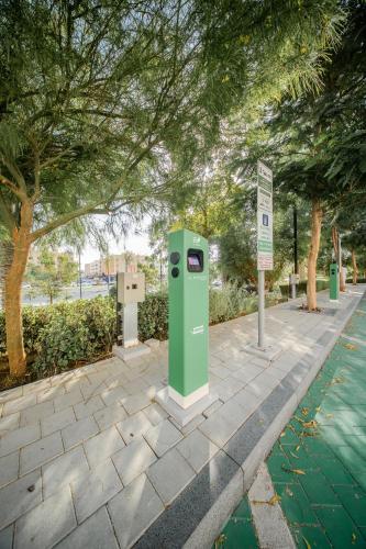 a green parking meter on a sidewalk next to trees at 1Bedroom & Living room Apartment - The Sahara Suite in Sharjah Intl
