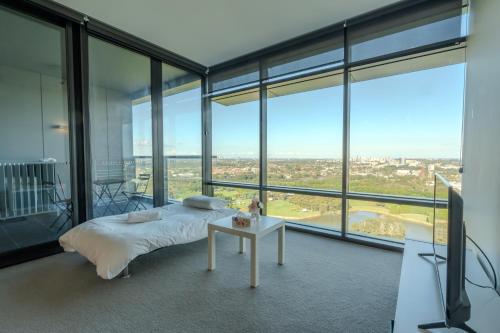 a bedroom with a bed and a table and windows at Modern Apartment with City View at Sydney Olympic Park in Sydney