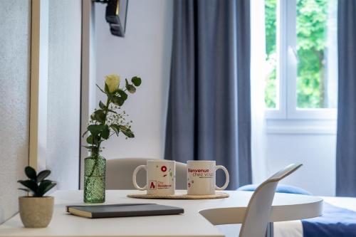 une table avec deux tasses à café et un vase avec des fleurs dans l'établissement City Résidence Strasbourg Centre, à Strasbourg