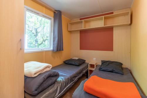 deux lits dans une chambre avec une fenêtre dans l'établissement Mobilhome avec terrasse 4 personnes, à Saint-Martial-de-Nabirat