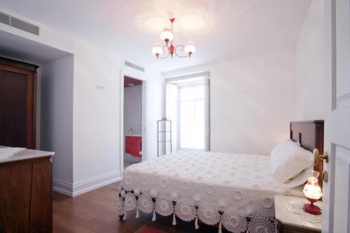 a white bedroom with a bed and a chandelier at Mercearia da Vila in Ponte de Lima