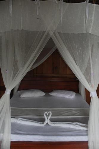 a bed with a canopy with white sheets and pillows at Malenge Dive Resort in Pulau Malenge