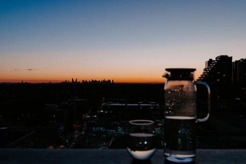 a bottle and two glasses sitting on a ledge with the sunset at Skyone Lux 2Bed room Aprt in BoxHill with car park in Box Hill