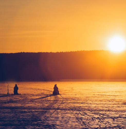 two people are sitting in the water at sunset at SKOG - Aurora Igloos Resort in Kalix