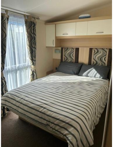 a bedroom with a bed with a striped comforter and a window at 15 Ivy Close, 3 Bedroom Caravan, Pet Friendly in Budleigh Salterton