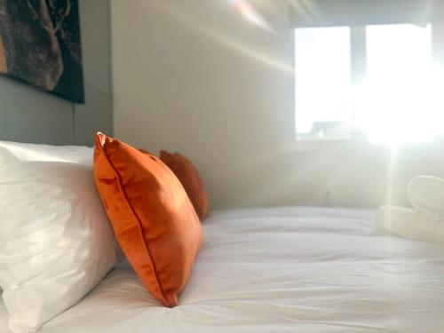 an orange pillow sitting on top of a white bed at Ruby Place by Blue Skies Stays in Hartlepool