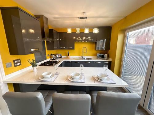 a kitchen with yellow walls and a counter with chairs at Mable House by Blue Skies Stays in Redcar