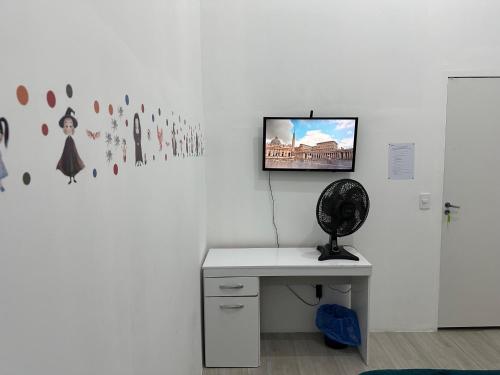 a white room with a desk and a tv on a wall at Quarto Sonserina Nº 1 in Sao Paulo