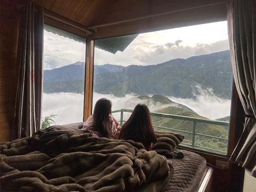 two girls sitting on a bed looking out of a window at Tà Xùa Retreat Khu Nghỉ Dưỡng in Bắc Yên