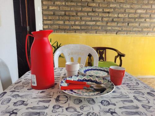 Una mesa con un jarrón rojo y un plato de comida. en Encanto potiguar sol e mar, en Natal