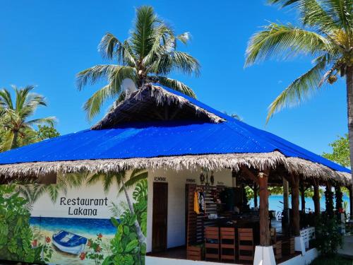 a restaurant with a blue roof and palm trees at Long Beach Resort, Nosy Be in Nosy Be