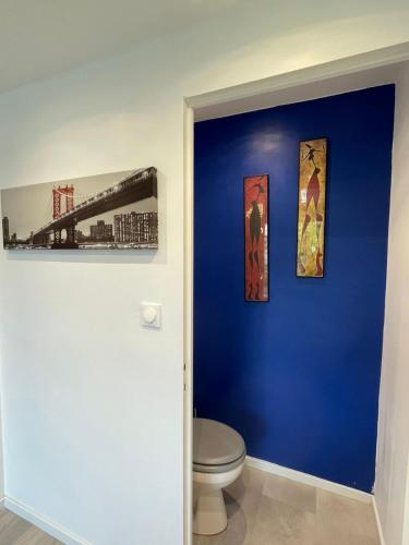 une salle de bain avec un mur bleu avec des toilettes et trois tableaux dans l'établissement Colorino - T4 Lumineux Cosy, Parking Gratuit, Commerces, à Saint-Brieuc