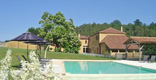 a swimming pool with an umbrella and a house at Domaine du Champ de l'Hoste in Larzac