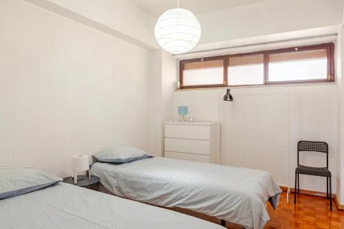 a bedroom with two beds and a window and a chair at Casa na Praia in Sesimbra