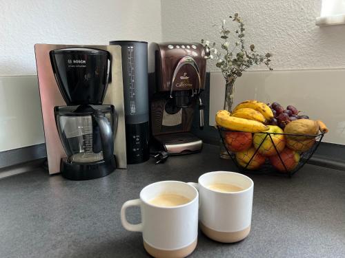 two cups of coffee and a basket of fruit on a counter at Ferienwohnung Schwarzwald Lodge in Schömberg