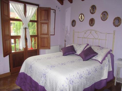 a bedroom with a bed with purple pillows and a window at Posada Rincón del Pas in Puente Viesgo