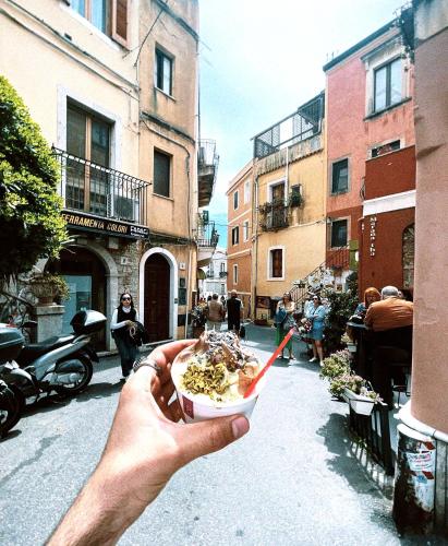 a hand holding a bowl of food on a street at Poet's rooms in Taormina