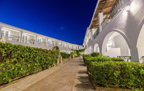 a walkway next to a white building with bushes at Sofia's Hotel in Kalamaki