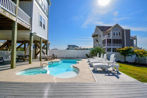 a swimming pool with white chairs and a house at Sounds Beachy in North Topsail Beach