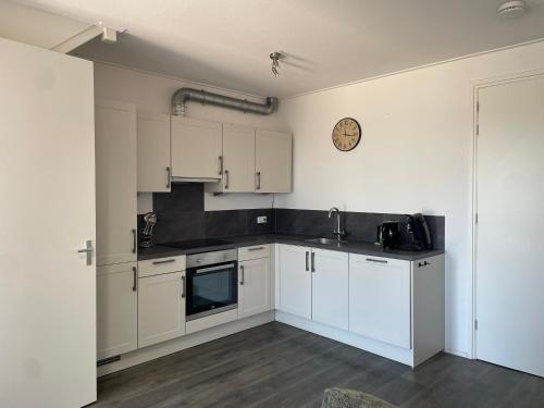 a kitchen with white cabinets and a clock on the wall at Nieuw gebouwd appartement op paarden bedrijf in Buitenpost