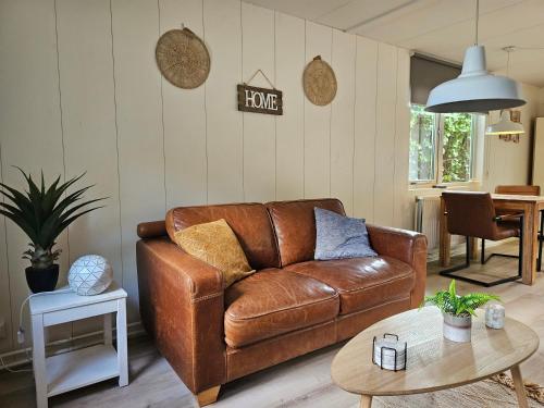 a living room with a brown leather couch and a table at Zomerhuis Duinzicht in Egmond aan den Hoef