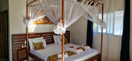 a bedroom with a canopy bed with white curtains at Long Beach Resort, Nosy Be in Nosy Be