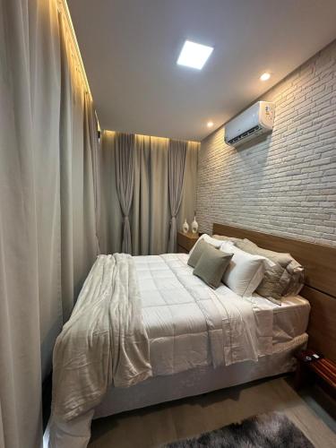 a bedroom with a white bed and a brick wall at Casa de Vidro na Montanha in Cambuí