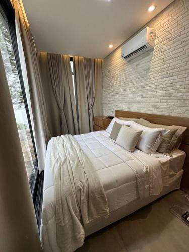 a bedroom with a white bed and a brick wall at Casa de Vidro na Montanha in Cambuí