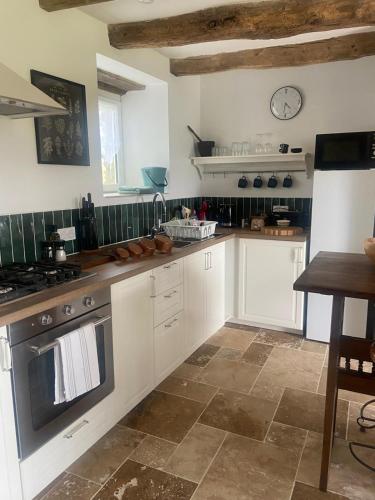 une cuisine avec des placards blancs et une horloge murale dans l'établissement Pinabre Rose Cottage, à Plouguenast Langast