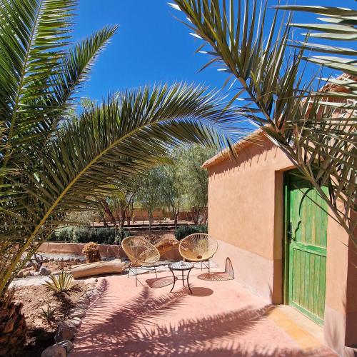 a patio with two chairs and a table and a palm tree at Maison d'hôtes Tigminou - Adults Only in Aït Ben Haddou