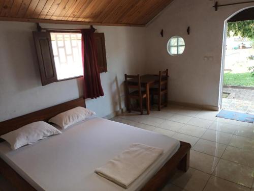 a bedroom with a bed and a table and a window at Hôtel-bungalows La Pirogue in Sambava