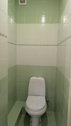 a white toilet in a bathroom with green tiles at Celtnieku 8 in Ventspils