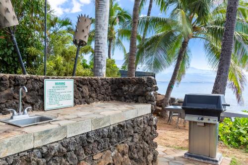 a stone wall with a grill and palm trees at Maalaea Banyans 416 by Coldwell Banker Island Vacations in Wailuku