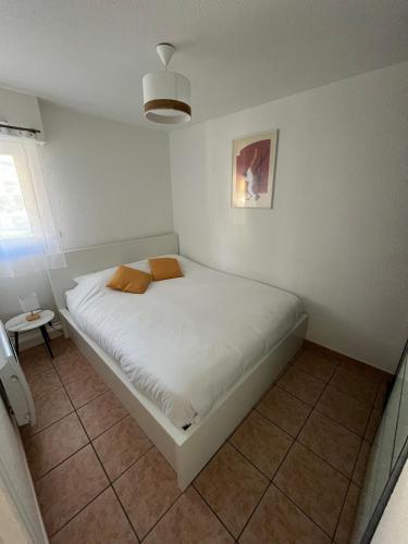 Cette petite chambre comprend un lit avec des draps blancs et des oreillers orange. dans l'établissement Entre océan et golf, à Anglet