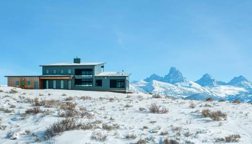a house on a snowy hill with mountains in the background at Luxury Retreat Epic Views & Hot Tub in Tetonia