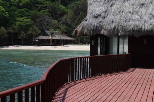 a boardwalk leading to a beach with a thatched building at Cauayan Island Resort and Spa in El Nido