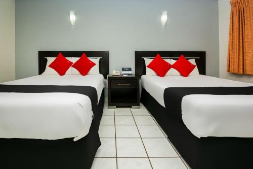 zwei Betten mit roten Kissen in einem Zimmer in der Unterkunft Capital O Hotel Victoria Morelia in Morelia