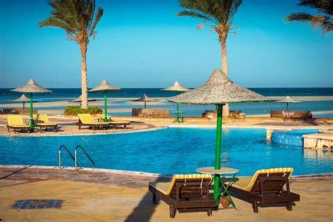 a swimming pool with chairs and umbrellas and the ocean at La Hacinda لا سيندا للعائلات in Ras Sedr