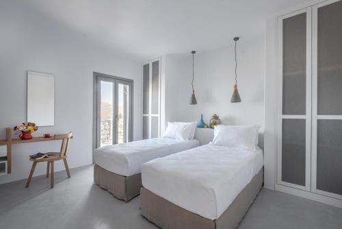 two beds in a bedroom with white walls and a table at Seven Suites in Glinado Naxos